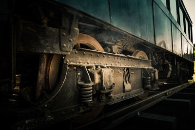 Bas d’un ancien tramway de Marseille avec roues métalliques, rivets, ressorts, rails et carrosserie sombre usée par le temps.