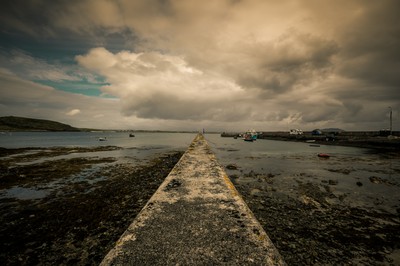 Jetée en pierre de Bunowen Pier dans le Connemara, avec mer à marée basse, petits bateaux et ciel nuageux en Irlande.