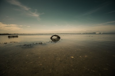 Paysage côtier à marée basse près de Dublin avec nasse en forme d’arche, reflet dans l’eau calme et voiliers au loin.