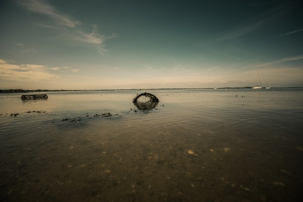 Paysage côtier à marée basse près de Dublin avec nasse en forme d’arche, reflet dans l’eau calme et voiliers au loin.