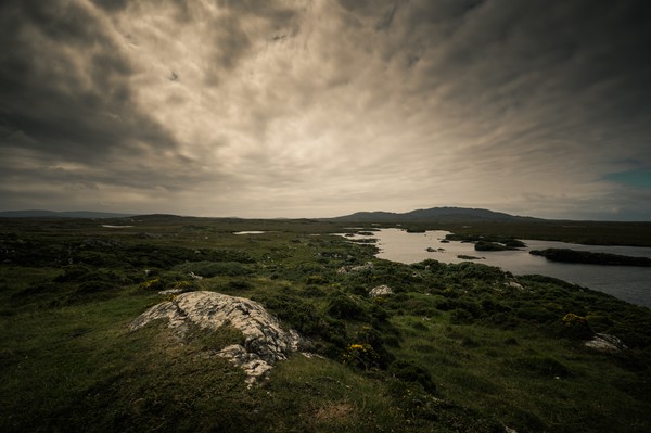 Paysage irlandais étendues d’eaux, collines verdoyantes, roche au premier plan et grand ciel chargé