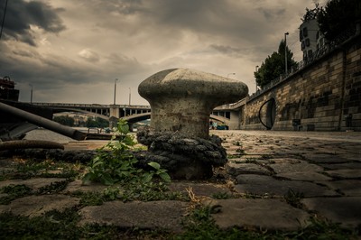 Photo d’art sur la Náplavka à Prague, montrant une amarre de quai au premier plan près du Jiráskův most, avec la Vltava et le Dancing House en arrière-plan.