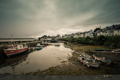 Bateaux de pêche à marée basse dans le port de Roundstone, maisons alignées au bord de l’eau et ciel chargé sur le Connemara