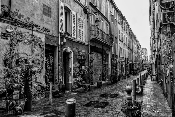 Rue Pastor près du Cours Julien à Marseille avec façades couvertes de graffitis, pavés humides et passants au fond.
