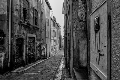 Rue étroite du quartier du Panier à Marseille, avec pavés, façades anciennes, graffitis et perspective urbaine en noir et blanc.